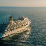 A breathtaking view of a cruise ship sailing across the ocean with the sun setting in the background.