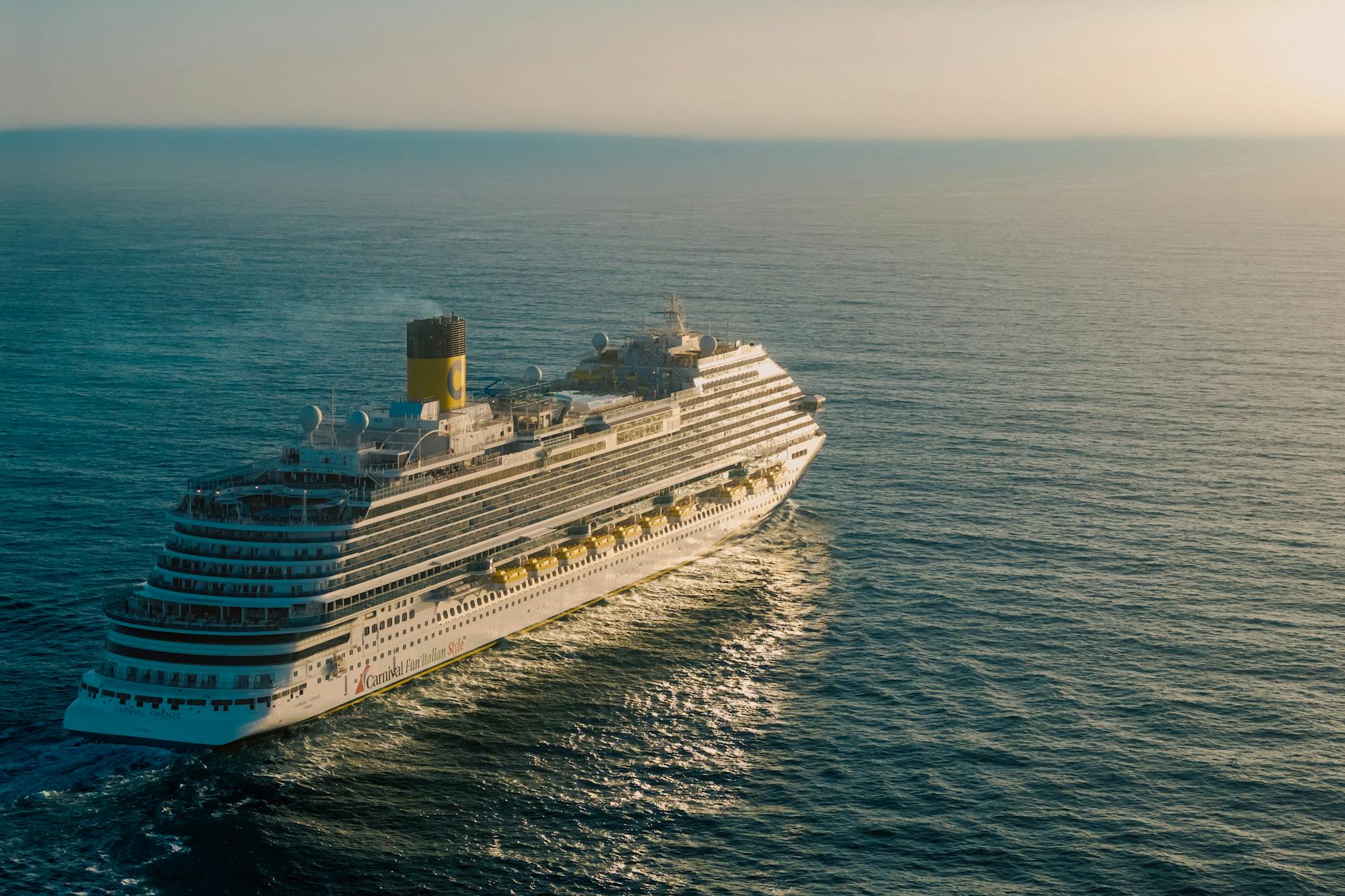 A breathtaking view of a cruise ship sailing across the ocean with the sun setting in the background.