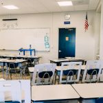 Bright empty classroom featuring desks, a whiteboard, and an American flag. Ideal learning environment.