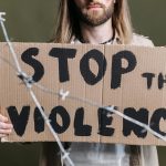 Close-up of a protester holding a cardboard sign reading 'Stop the Violence' with barb wire in focus.