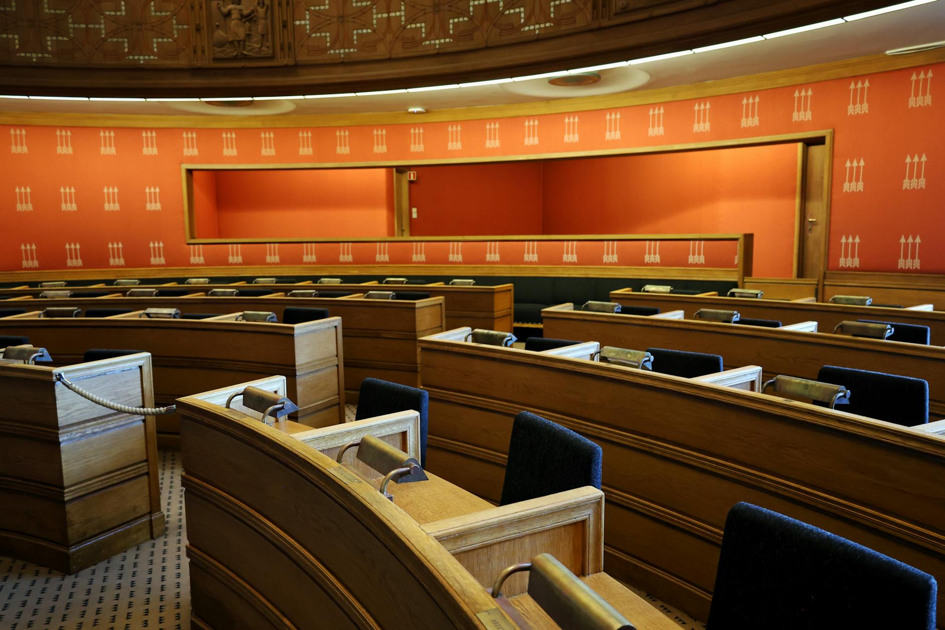 An empty parliamentary meeting room with wooden seating and vibrant orange walls in Oslo, Norway.