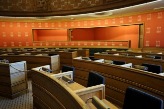 An empty parliamentary meeting room with wooden seating and vibrant orange walls in Oslo, Norway.